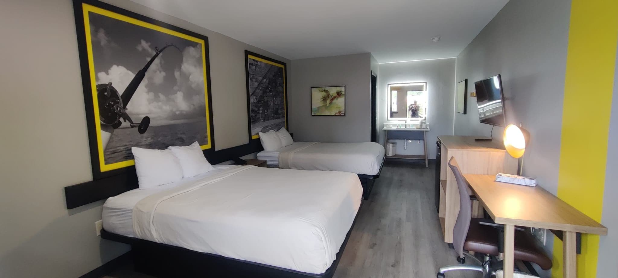 Habitación de hotel con dos camas, un escritorio, una silla, un televisor y obras de arte en las paredes.