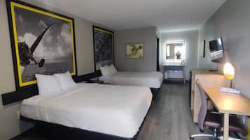 Habitación de hotel con dos camas, un escritorio, una silla, un televisor y obras de arte en las paredes.