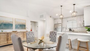 A modern kitchen with white cabinets, a stainless steel refrigerator, and a glass dining table with four chairs. - Private Cottage at PGA National (Palm Beach Gardens)