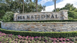 A stone wall with "EGA NATIONAL" engraved on it, surrounded by landscaped gardens and palm trees. - Private Cottage at PGA National (Palm Beach Gardens)