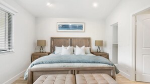 A bedroom with a large bed, two bedside tables, a bench, a window with blinds, and a painting on the wall. - Private Cottage at PGA National (Palm Beach Gardens)