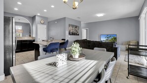 A modern dining area with a large table, chairs, and a chandelier. There is a kitchen area with cabinets and a refrigerator visible in the background. - ✨ Luxurious 6BR Villa with Private Pool & Game Room near Disney 🏊‍♂️🎮 (Davenport)