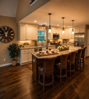 A spacious kitchen with a central island, wooden bar stools, and pendant lighting.