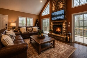 A living room with a stone fireplace, leather sofa, and large windows. - Luxury Chalet Masthope Near Narrowsburg & Delaware (Masthope)