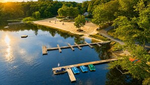 Un muelle en la orilla de un lago con barcos, una zona de arena y árboles.