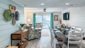 Un comedor con una mesa de madera dispuesta para cuatro personas, un sofá y un televisor montado en la pared.