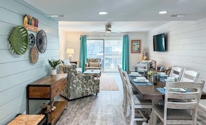 Un comedor con una mesa de madera dispuesta para cuatro personas, un sofá y un televisor montado en la pared.