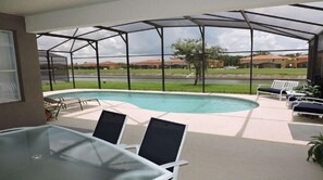 Un'area esterna coperta con piscina, sdraio e tavolo in vetro.