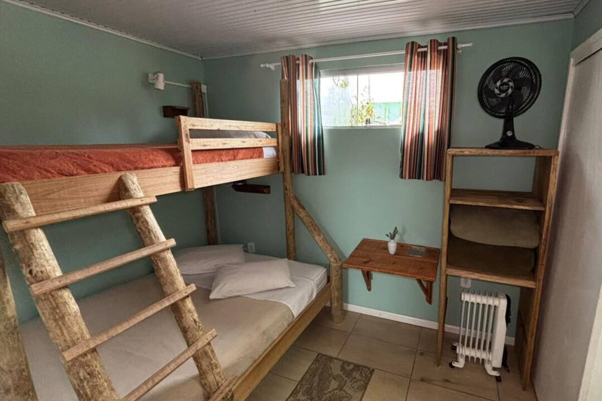 A bunk bed room with a wooden ladder, a small table, a fan, and a radiator.