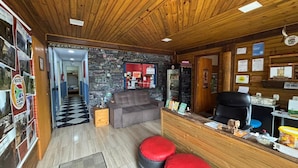 Interior de un hostal con suelo de cuadros, un sofá, mostrador de recepción y una pared con diversos carteles y letreros.