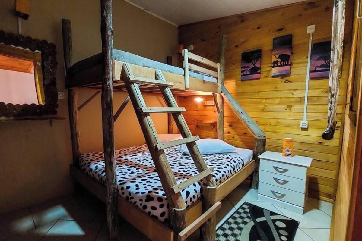 A bunk bed with a ladder, a small bedside table, a mirror, and a window.