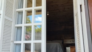 Puerta francesa abierta que da a una habitación con cama, techo de madera y una mesita.