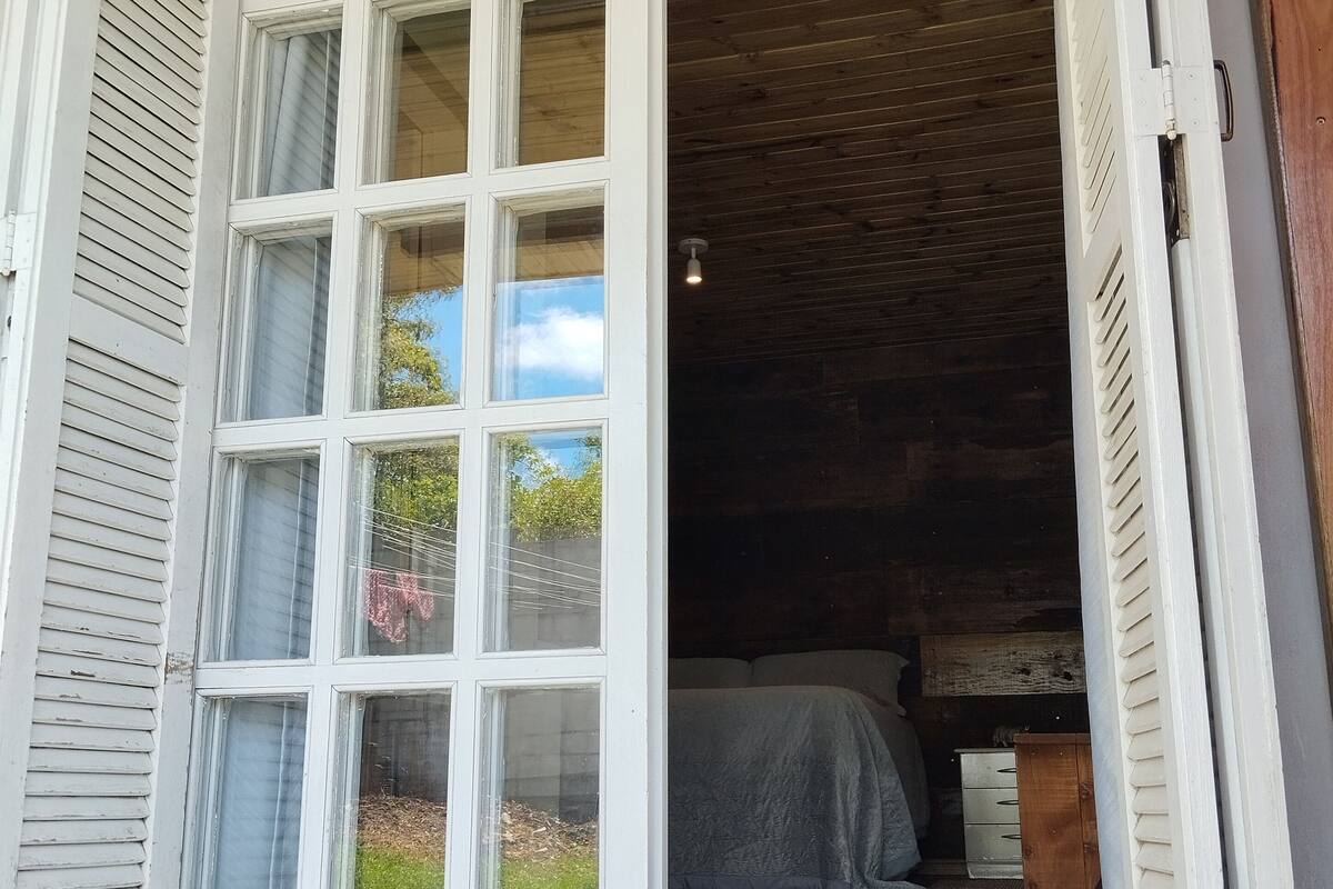 An open French door leading into a room with a bed, wooden ceiling, and a small table.