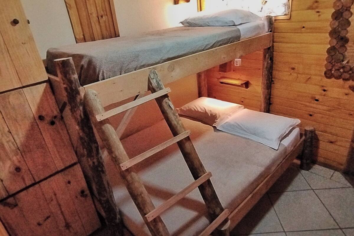 A bunk bed with a ladder, wooden walls, and a small shelf.