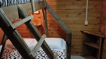 Una habitación tipo cabaña de madera con una litera, un estante pequeño y un aplique en la pared.