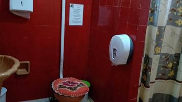 Une salle de bain équipée de toilettes, d’un sèche-mains, d’un distributeur d’essuie-tout, d’un distributeur de savon liquide et d’un rideau de douche.