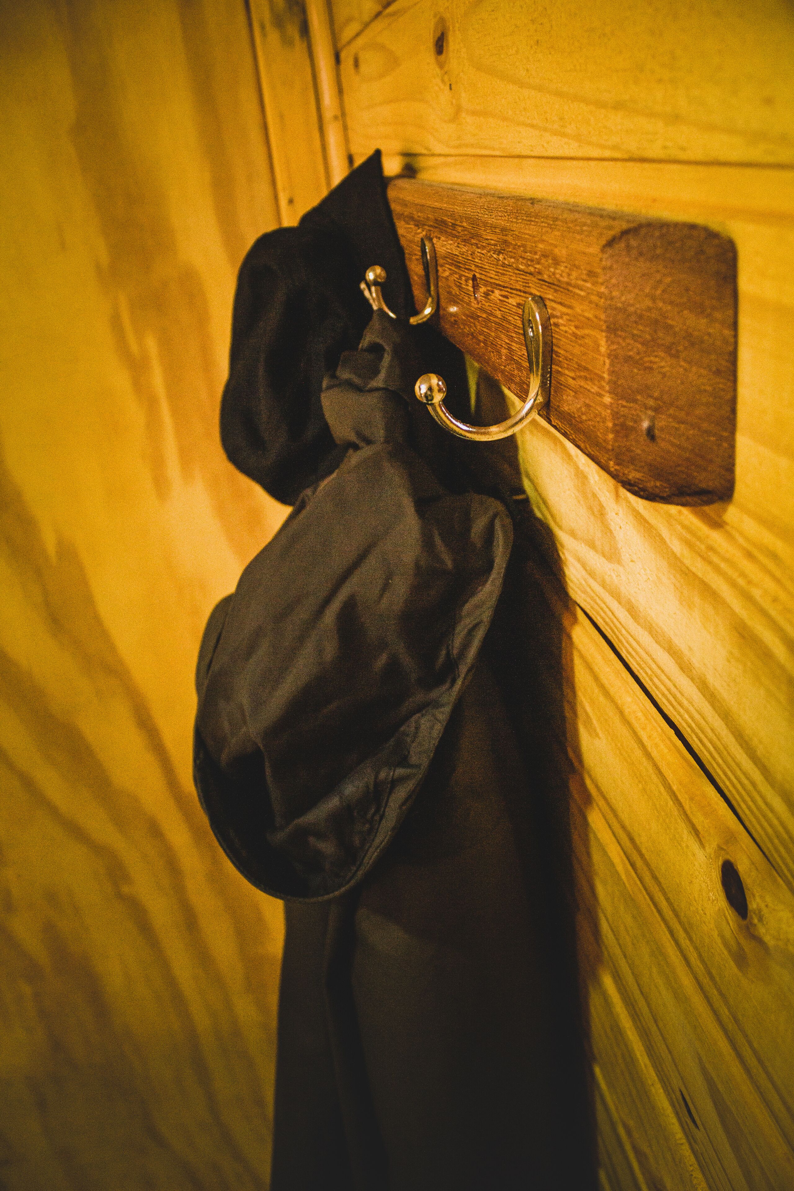 Eine Holzwand mit einem Kleiderhaken, an dem zwei schwarze Mäntel hängen.