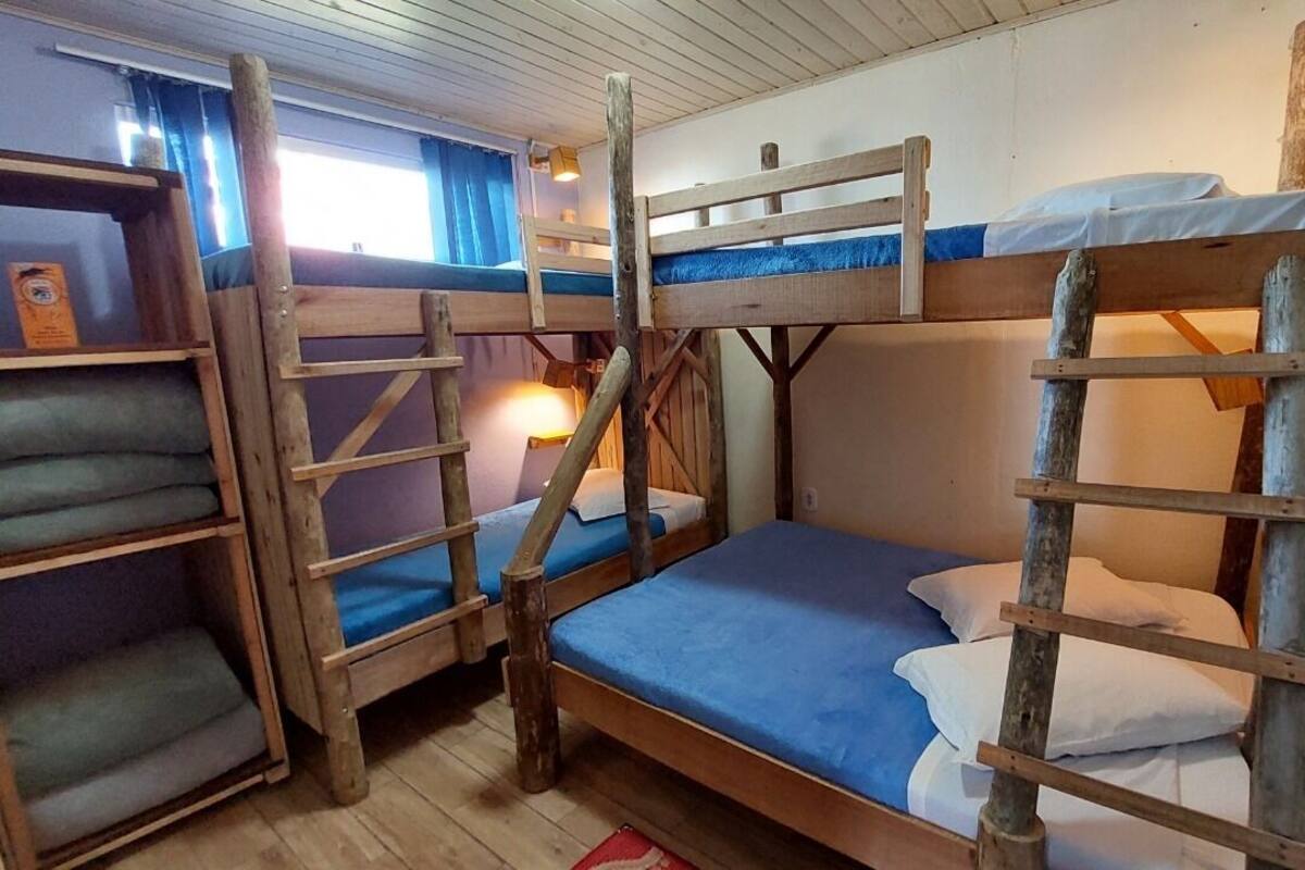 A bunk bed room with wooden railings and a ladder, a shelf with a book, and a window with curtains.