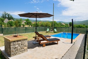Um quintal com piscina, espreguiçadeiras, um banco de pedra e um guarda-sol.