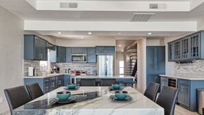 A modern kitchen with dark blue cabinets, a large island with seating, and a marble dining table. - Luxury Beachfront Six Palms Villas # 1 (Puerto Penasco)