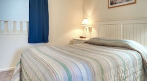 Un dormitorio con una cama, una mesita de noche, una lámpara y una ventana con cortina azul.