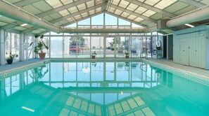 Una piscina interior con paredes de vidrio transparente, suelo de baldosas y estructura de techo.