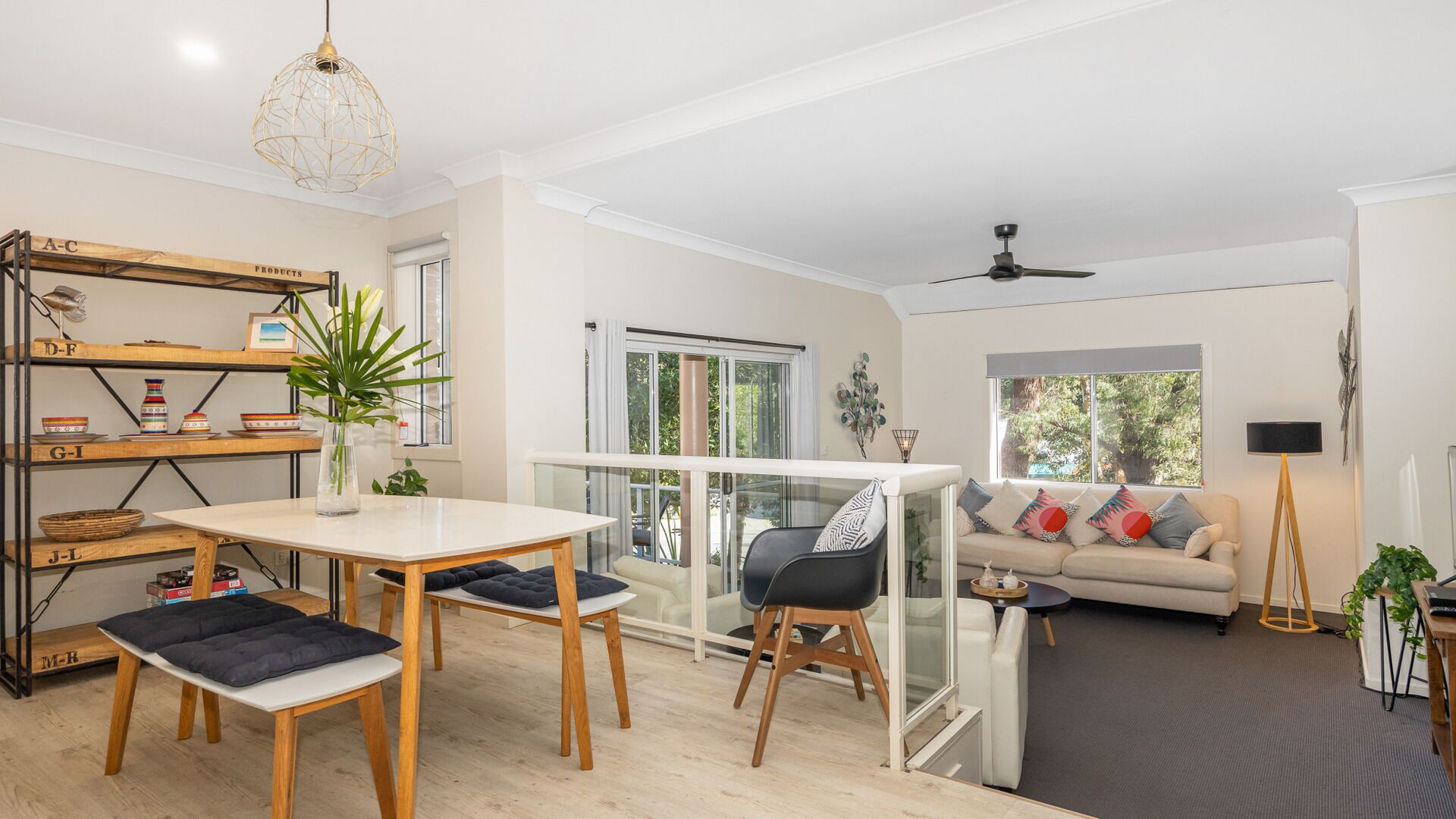 Un salon moderne doté d’un coin repas avec une table en verre, d’un canapé agrémenté de coussins colorés et d’un ventilateur de plafond.