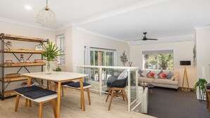 Un salon moderne doté d’un coin repas avec une table en verre, d’un canapé agrémenté de coussins colorés et d’un ventilateur de plafond.