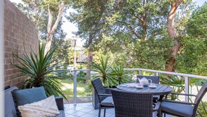 Une terrasse extérieure avec des meubles en osier, une table avec une théière et des plantes en pot.