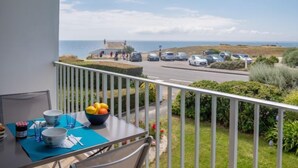 Een balkon met een ontbijttafel, met uitzicht op een parkeerplaats en de zee.