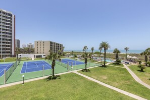 Un complexe de courts de tennis doté d’une piscine, de palmiers et offrant une vue sur l’océan.