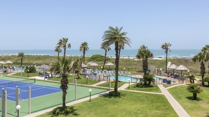 A beachside resort with a tennis court, pool area, and beach chairs.