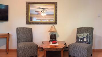 A living room with two grey armchairs, a wooden coffee table, a lamp, a framed picture, and a ceiling fan.
