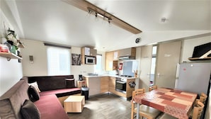 A compact living space with a sofa, a dining table, a kitchen area with a stove, microwave, and refrigerator. - Mobile home near the beaches (Saint-jean-de-monts)