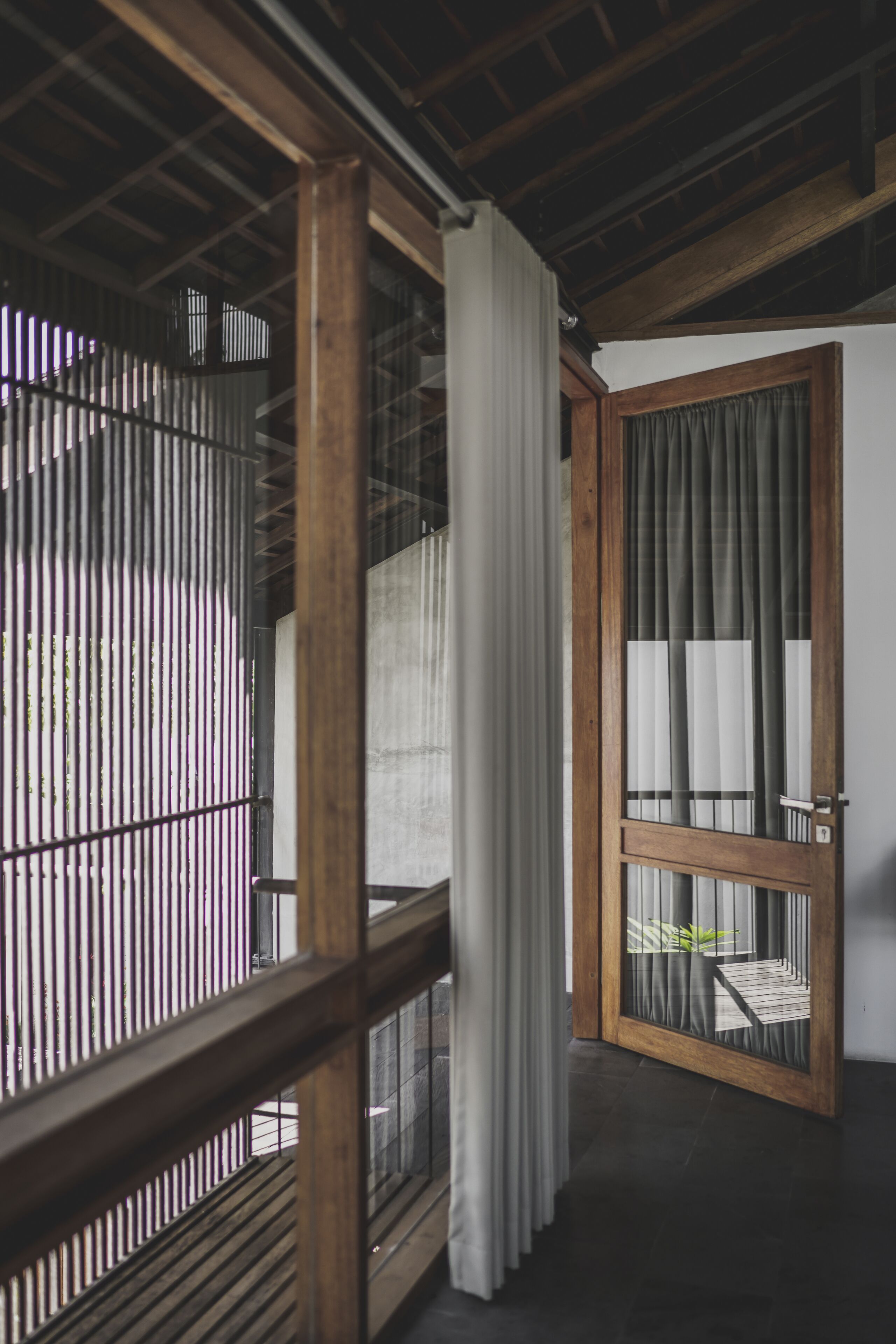 A room with a wooden ceiling, a sliding glass door with curtains, and a view of a balcony with vertical blinds.