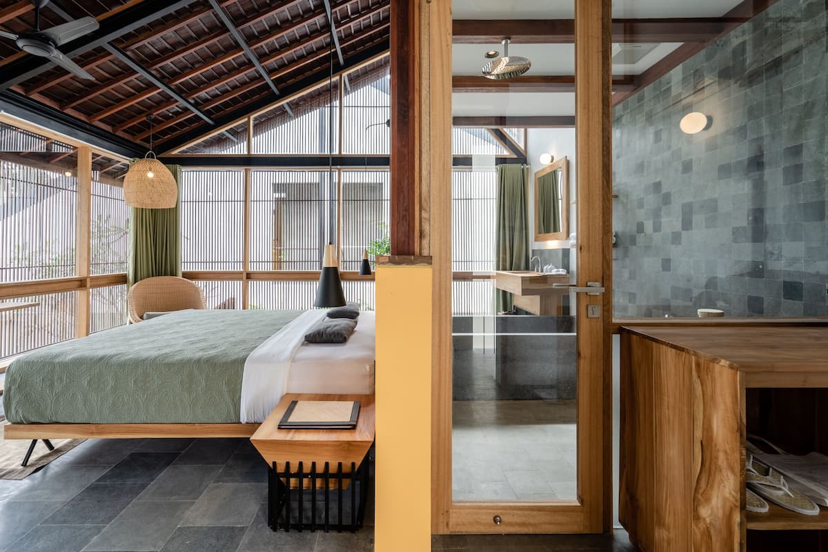 A modern bedroom with a bed, bedside table, and a view through a glass door to a bathroom.
