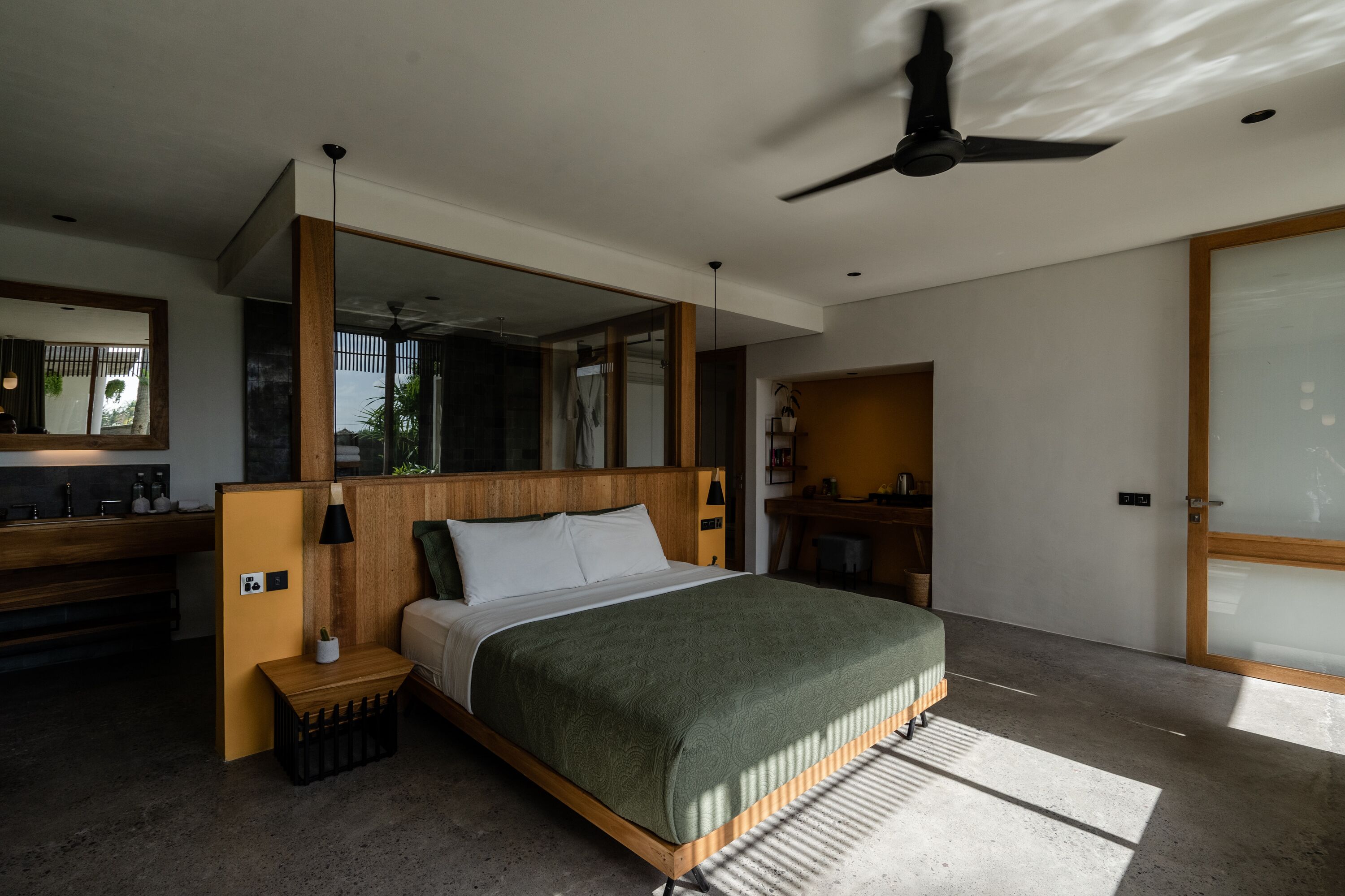 Een moderne slaapkamer met een groot bed, een plafondventilator, een houten hoofdbord, een nachtkastje met een lamp en een grote spiegel.