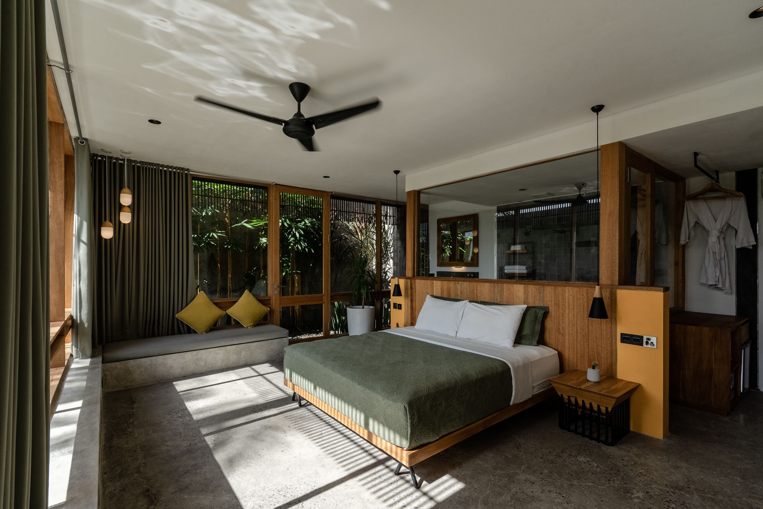 Une chambre moderne avec un grand lit, un ventilateur de plafond, une tête de lit en bois, une table de chevet et un grand miroir.