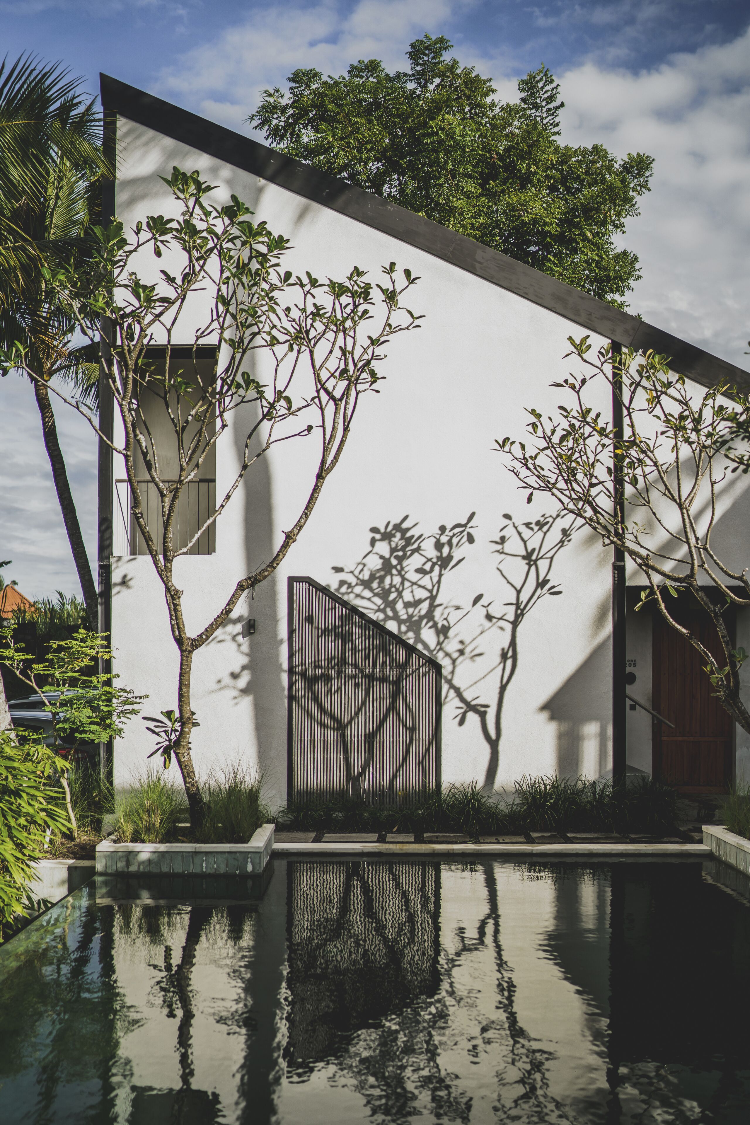 A modern building with a white exterior, a reflective pool, and a gated entrance.