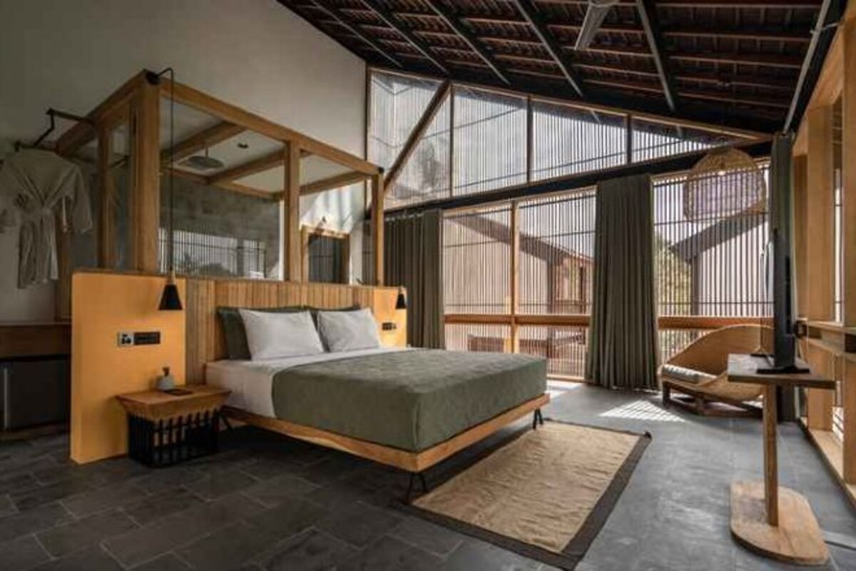 Une chambre à coucher avec un grand lit, une tête de lit en bois, une table de chevet et un coin salon comprenant une chaise et une table.