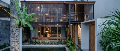 A modern two-story house with a pool, wooden deck, and lush greenery.