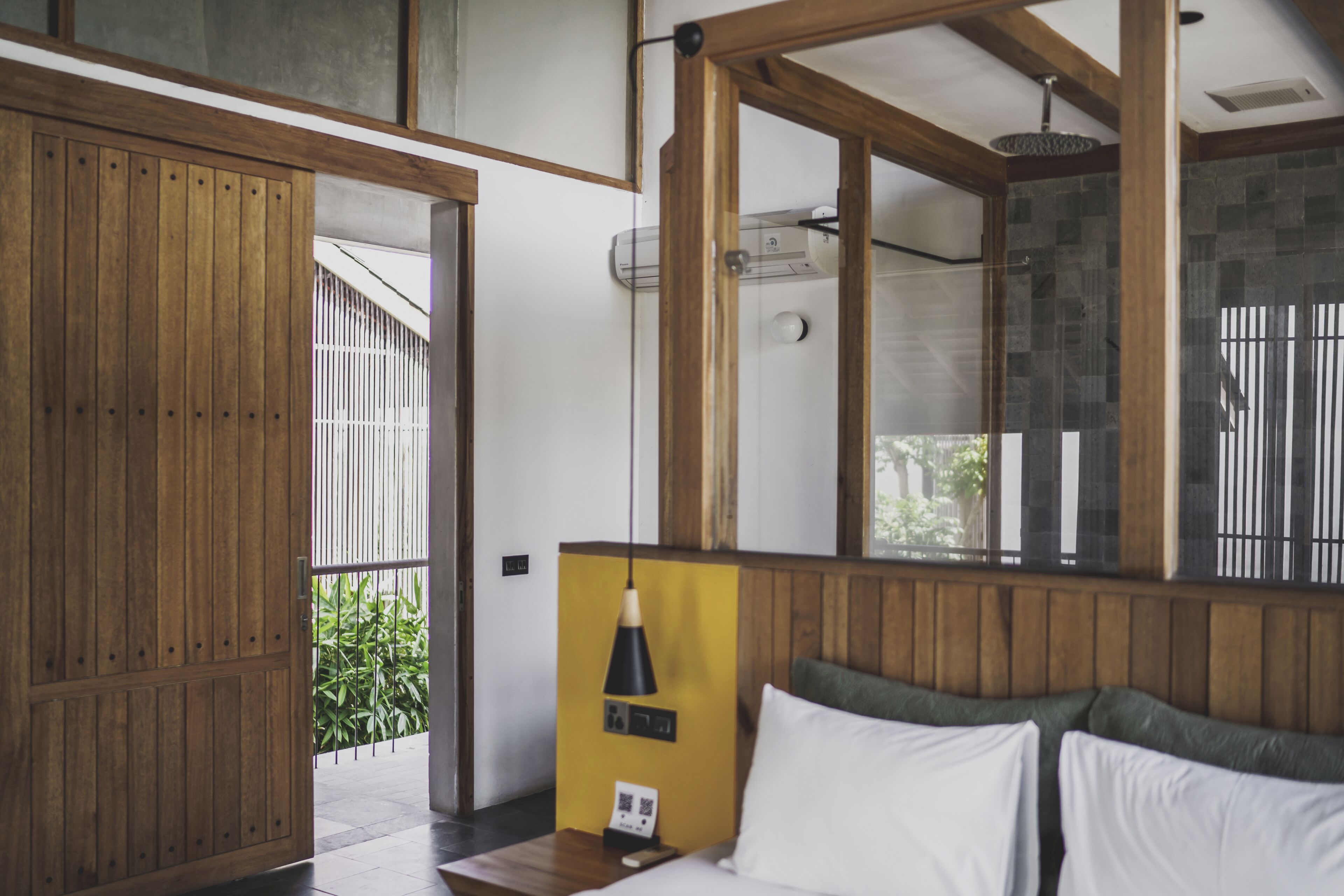 Una habitación con un armario de madera, una cama con ropa blanca, una pared amarilla y un espejo grande que refleja una zona de ducha.