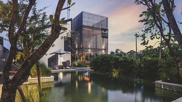 A modern building with a glass facade, surrounded by lush greenery and a calm water body. - The Saren (Tabanan)