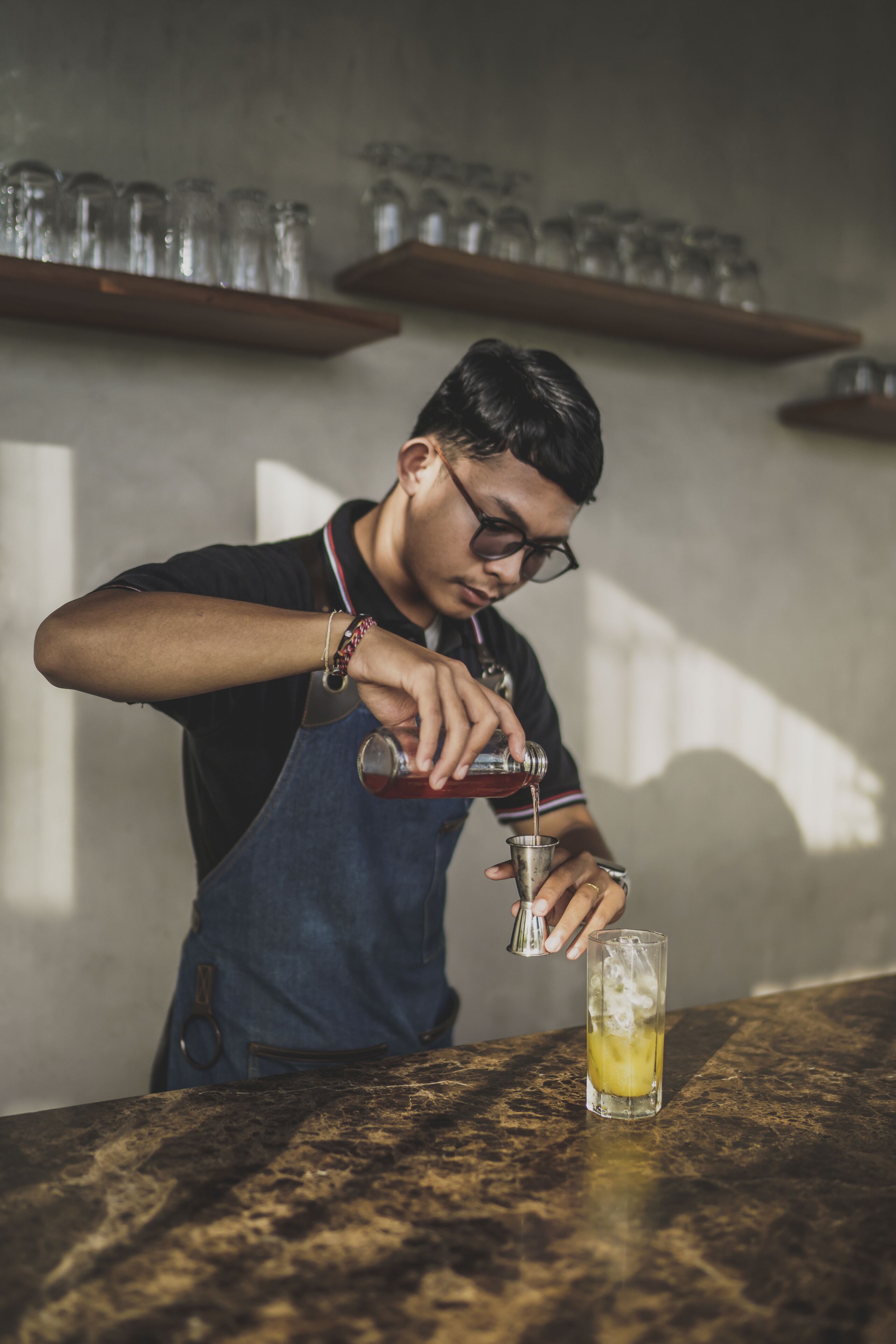 A person pouring a drink into a glass on a bar counter.