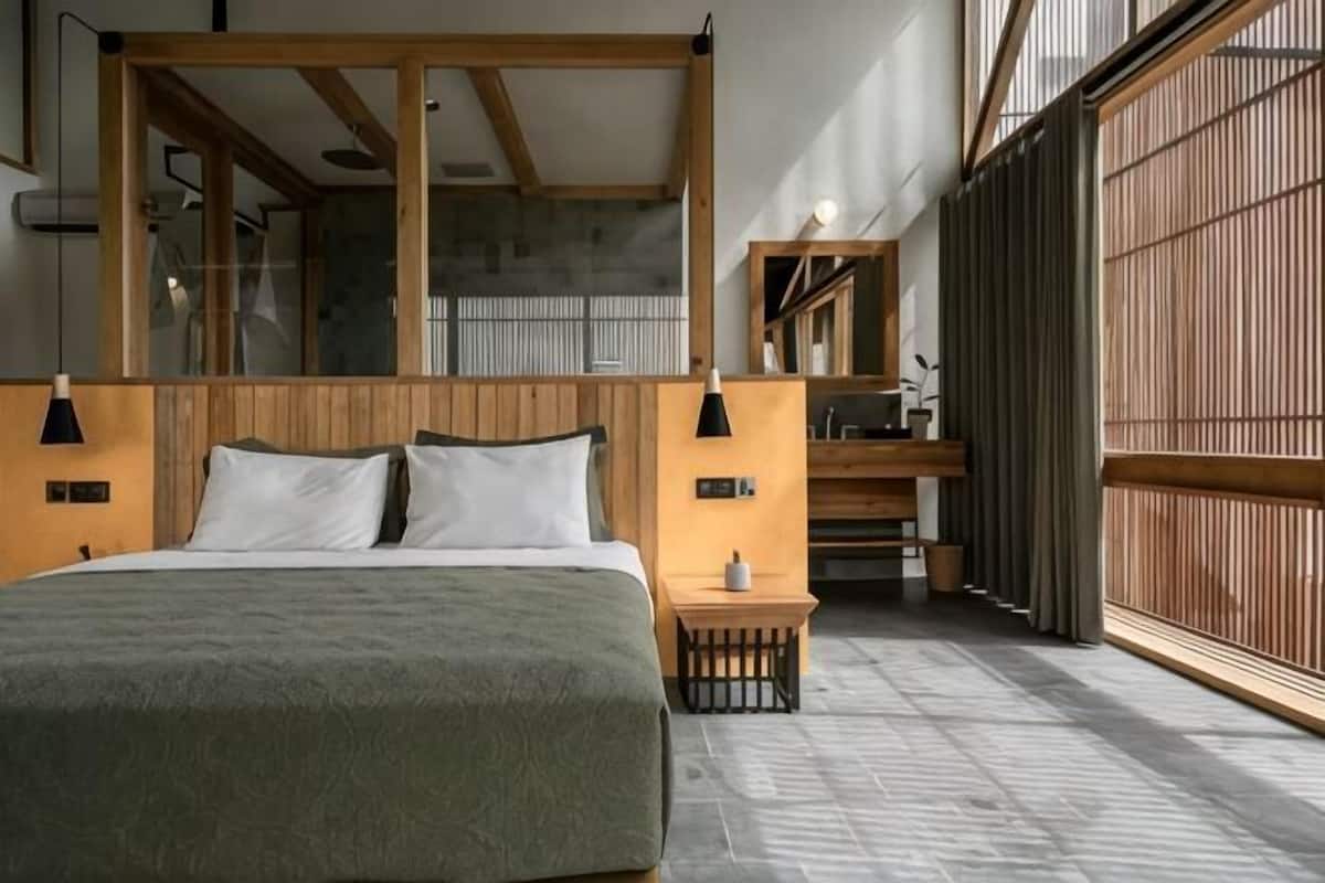 A bedroom with a large bed, wooden headboard, bedside tables, a small nightstand, and a view through a sliding door.
