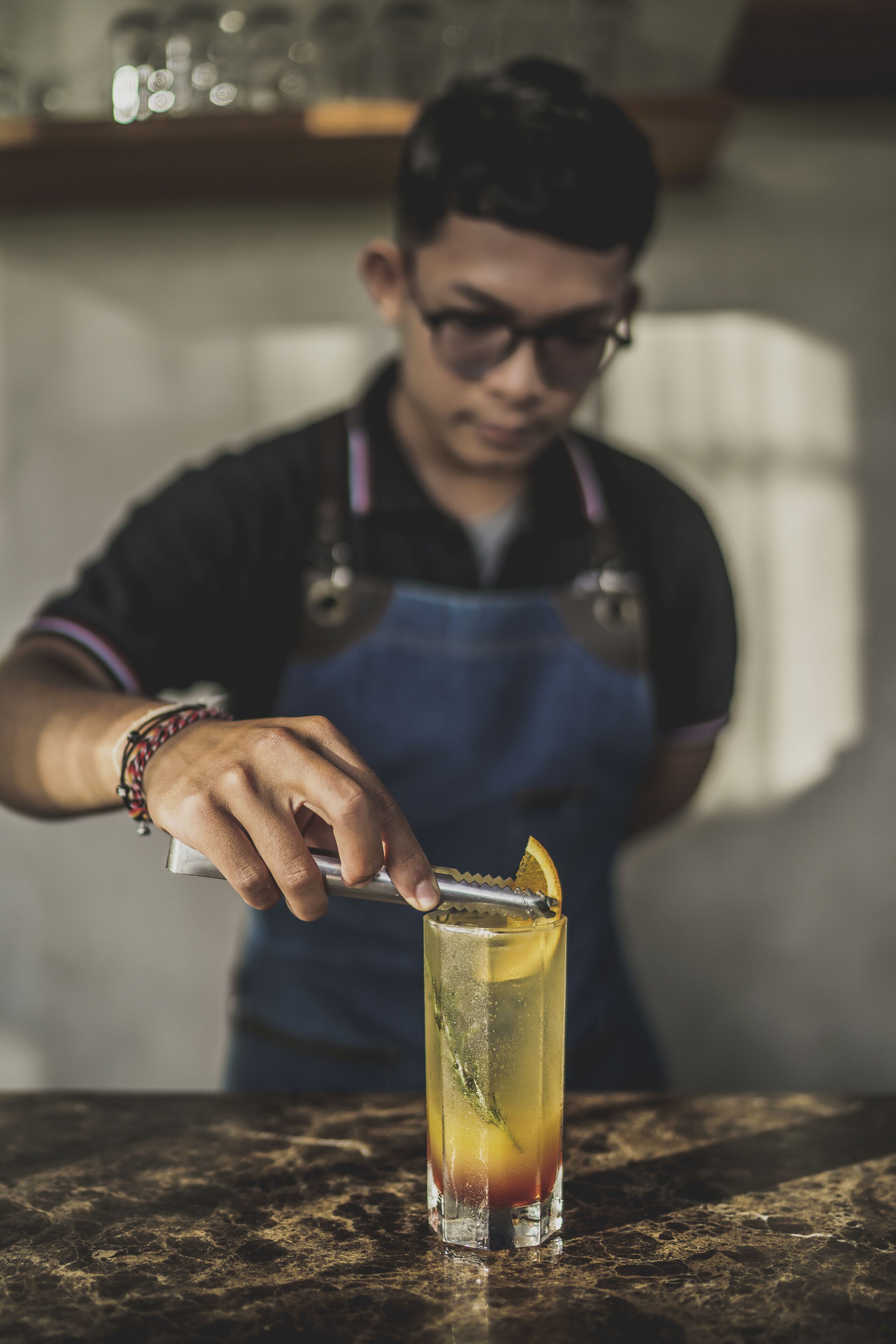 En person i sort skjorte og blå forklæde laver en drink med citrusfrugt.