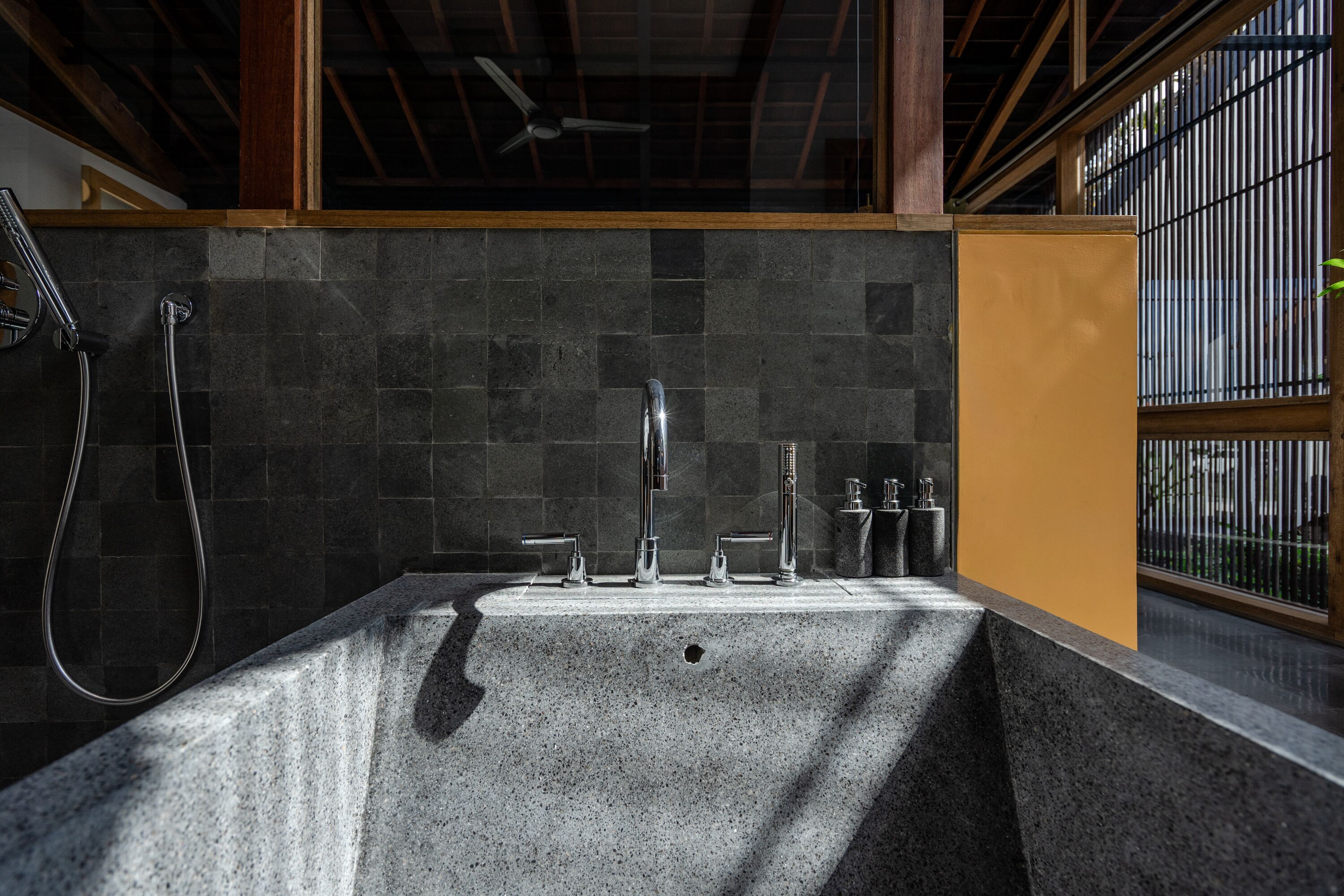 A bathroom with a granite sink, multiple faucets, and a showerhead.