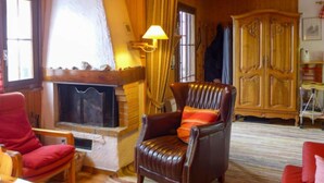 Ein gemütliches Wohnzimmer mit Kamin, Ledersessel, Holzschrank und einem roten Sofa.