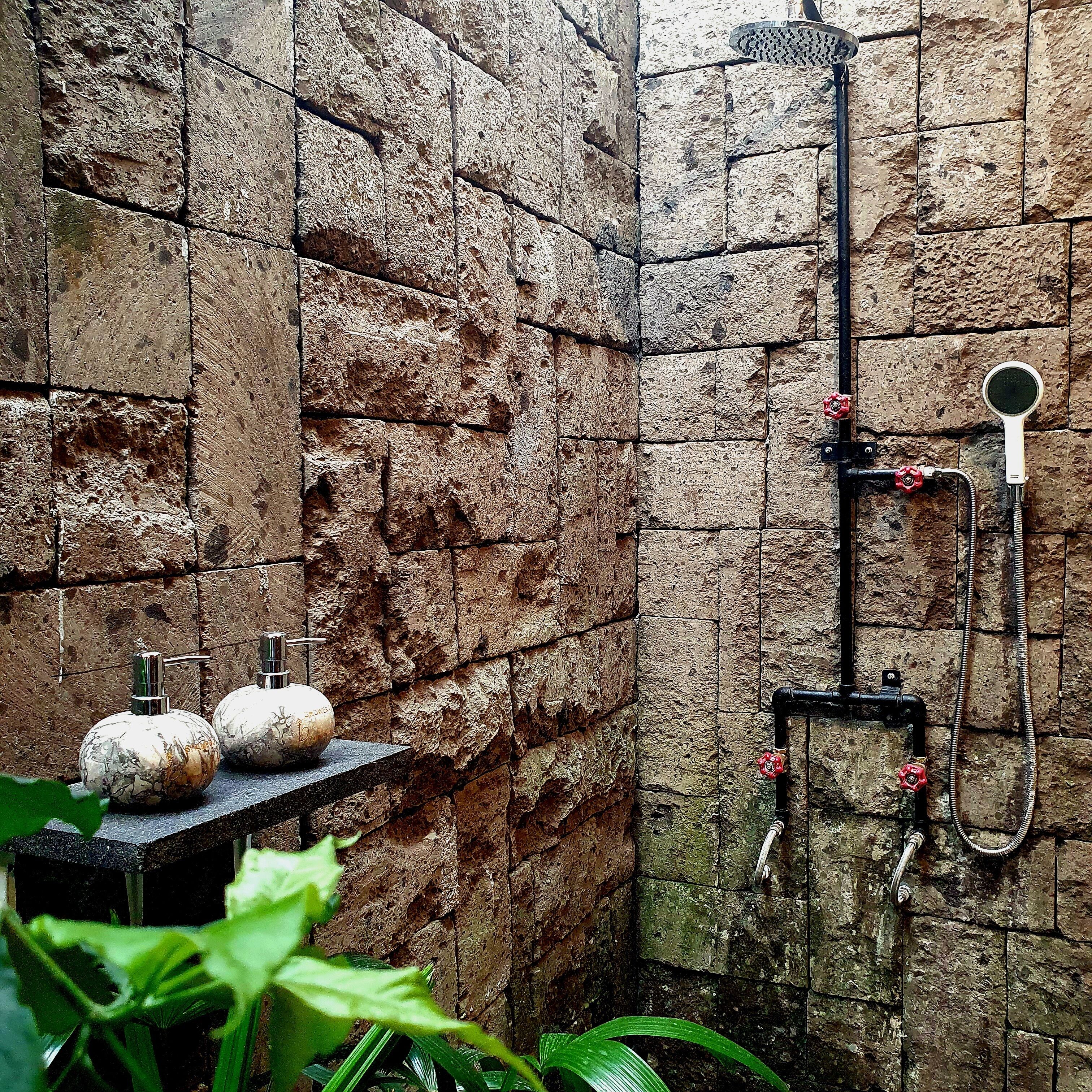 A bathroom with stone walls, a shower with a handheld mirror, and two decorative pumpkins on a shelf.
