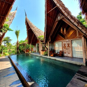 A poolside area with a wooden deck, a pool, and traditional-style buildings with thatched roofs. -  Premadhan Sanctuary (Pererenan)